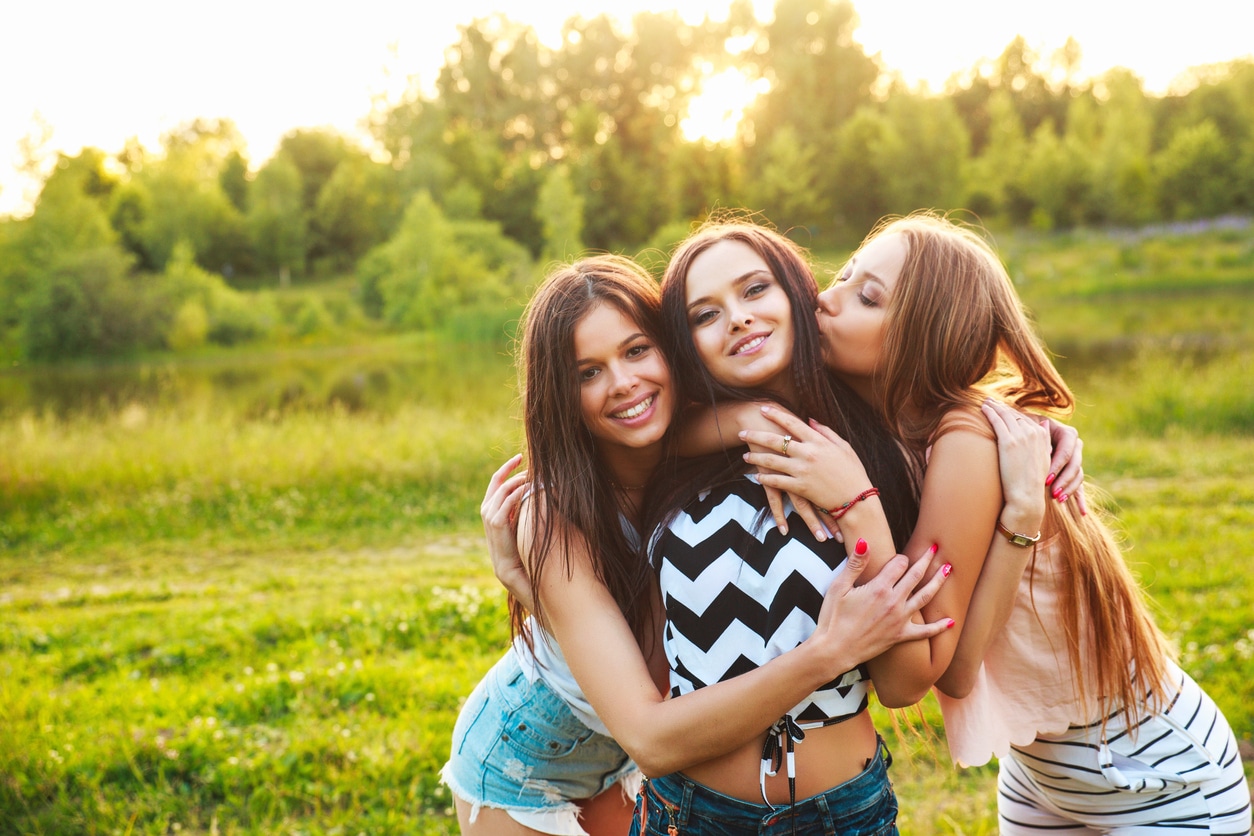 Three sisters walking and laughing on sunset in the park.